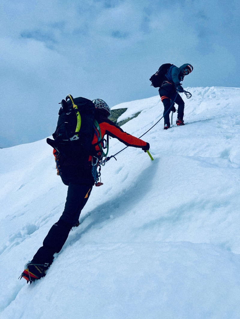 Two roped men climbing up a steeped bank of snow.