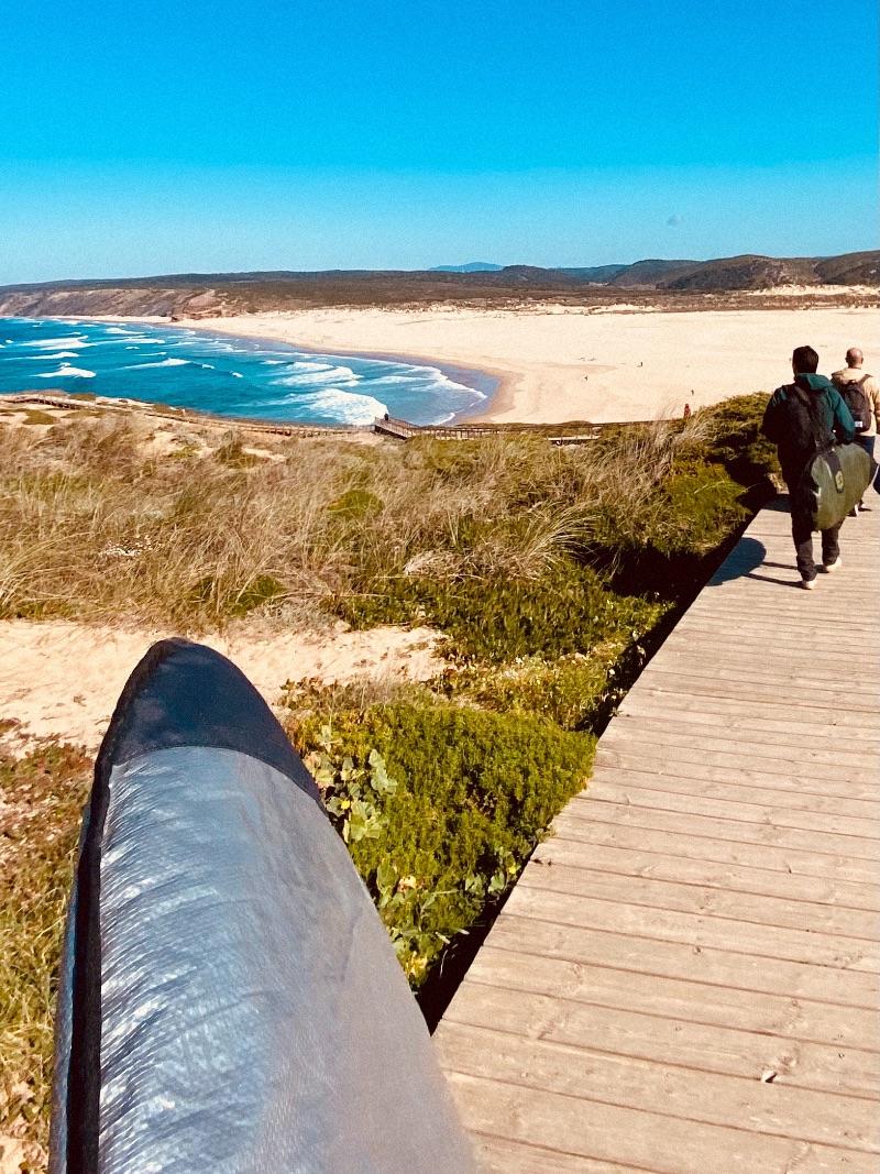 Walking down a wooden pathway with a surfboard towards the ocean.