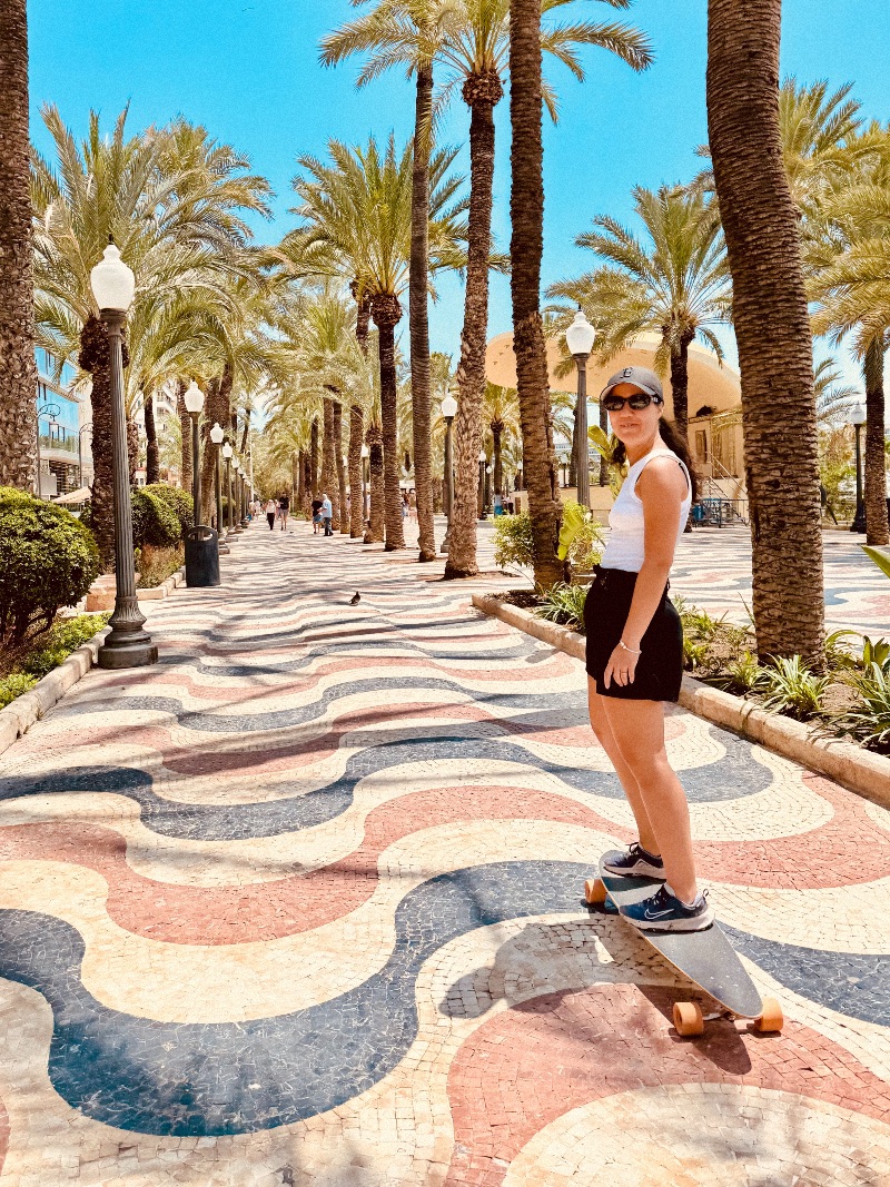 A girl looking back while skating on a longboard surrounded by palm trees.