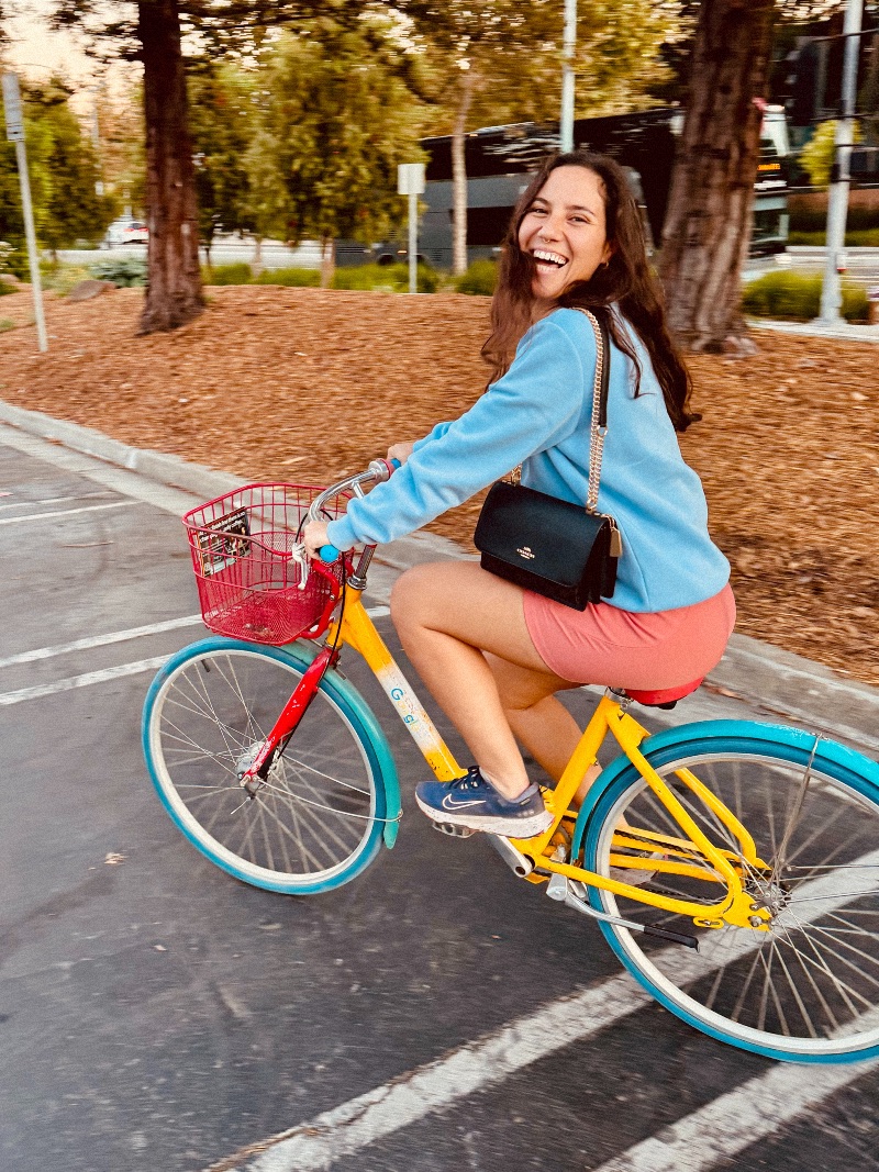 A girl riding a colorful Google bike while laughing at the camera.