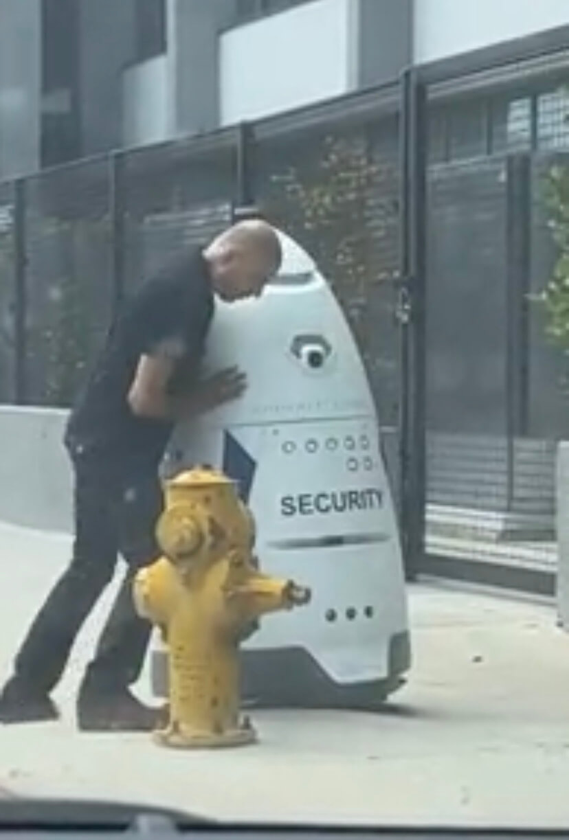 Someone pushing a security robot that is stuck on the sidewalk.